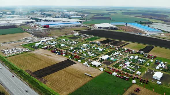 Drone Shot with Ascending Top View of Agricultural Expo Fair on Green Fields of Farm Lands with Fact alt