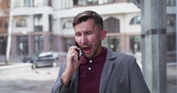 Portrait of Man Talks on the Phone and Sneezes Strongly Near Office Centre alt