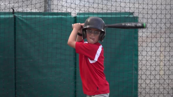 A boy practices baseball at a batting cage. alt