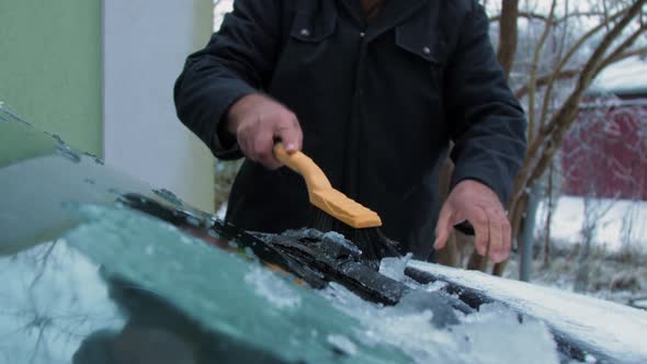 Person Holds Brown Wooden Snow Brush and Cleans Ice alt
