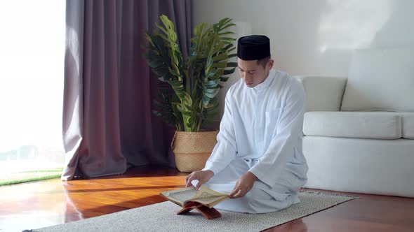 Young Muslim man wearing Islamic clothes reading the Quran alt