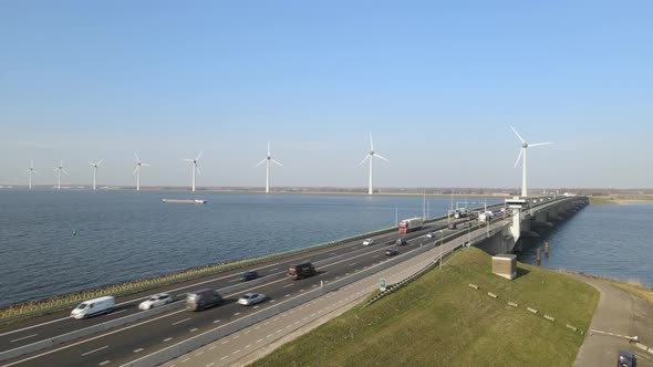 Aerial upwards revealing scenic bridge over water, traffic on road, windfarm on lake shore, Ketelbru alt