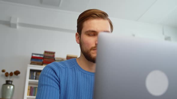 Smiling young man using laptop, studying online, working from home, typing on laptop alt