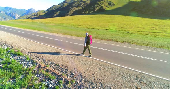 Flight Over Hitchhiker Tourist Walking on Asphalt Road. Huge Rural Valley at Summer Day. Backpack alt