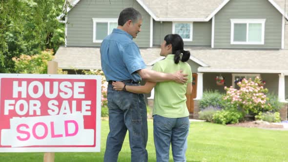 Couple look at new home, SOLD sign in foreground alt