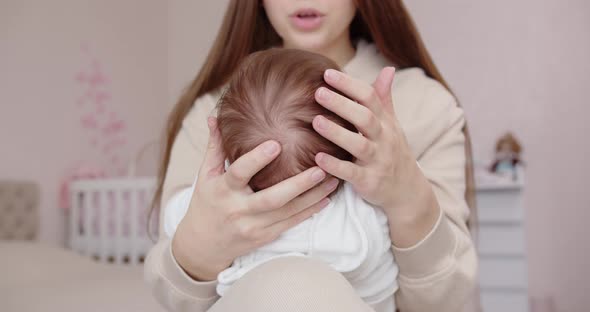 A Young Mother Holds Her Newborn Baby On Her Lap And Gently Strokes Her Small Head