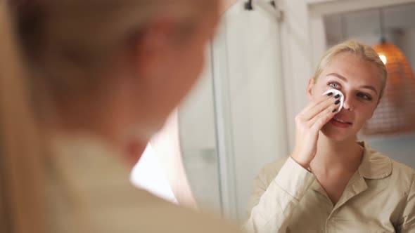 Positive blond woman wiping her face with a sponge at mirror alt