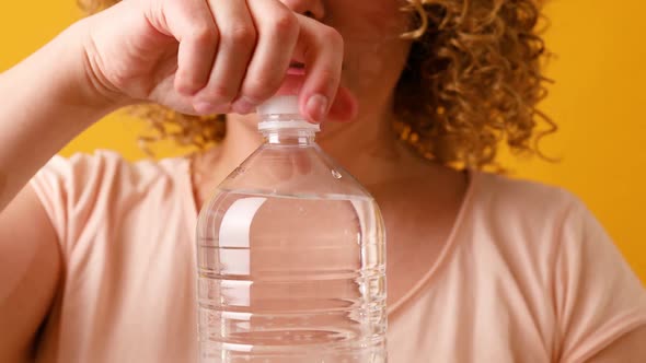 Happy Beautiful Young Woman with Curly Fluffy Hair Drinking Glass of Water Over Yellow Background