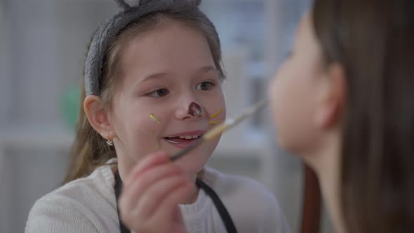 Joyful Little Girl Painting Sister Face with Food Coloring Smiling Enjoying Easter Fun alt