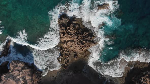 Top-down lowering over ocean waves crashing on rocky coast near Porto dos Frades, Madeira alt
