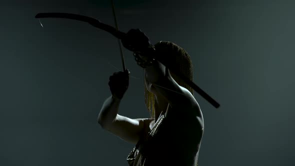 Silhouette of Dancing Joan of Arc with Bow and Arrow on Stage in a Dark Studio with Smoke and Neon alt