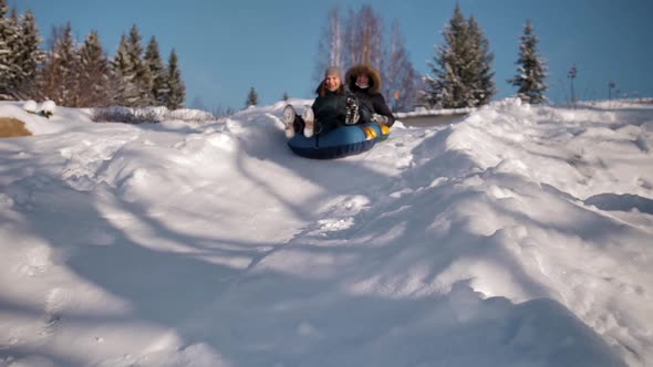 A Young Couple a Guy and a Girl are Riding a Snowtube From the Mountain alt