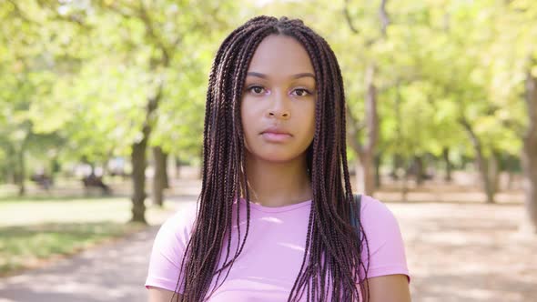 A Young Black Woman Looks Seriously at the Camera in a Park on a Sunny Day - Closeup alt