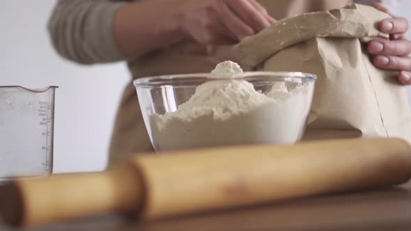 Chef girl puts flour with wooden spoon from paper bag in glass bowl. Measuring glass measuring spoon alt