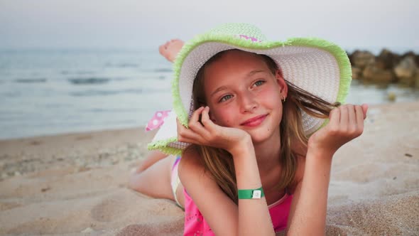 Portrait of Teen Girl in Hat is Dreaming Lying on the Sea Sand Beach