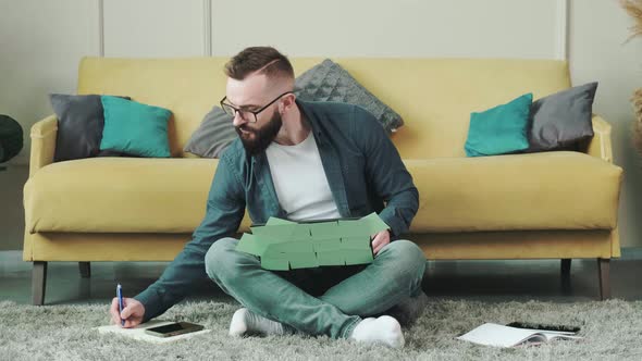 Man Working at the Computer with a Lot of Reminder Notes Sitting Near Sofa alt