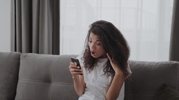 Young African American Lady Shocked and Frustrated Looking at Phone Seeing Bad News Photos Text alt
