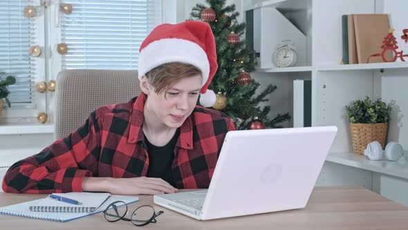 A Teenage Boy in a Santa Hat Talks Online Via Video Link on a Laptop with Friends or Relatives on