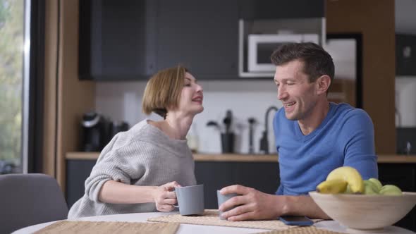 Happy Smiling Loving Husband Putting Away Smartphone Talking with Charming Wife Sitting Down at alt