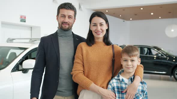 Slow Motion of Happy Family with Son Smiling in Car Dealership Standing Together alt