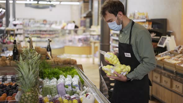 Male Assistant in Supermarket Food Store Worker in Medical Mask and Apron Arranges Packed Products alt
