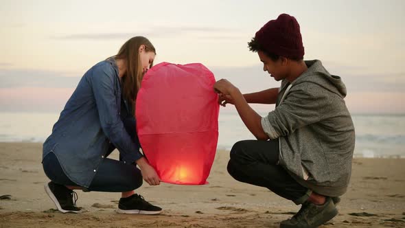 Cute Multiethnic Couple Holding Red Paper Lantern Before Launching alt