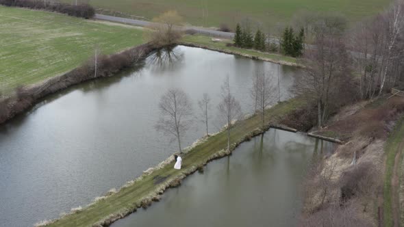 Newlywed couple walking on narrow pathway between lakes in autumn. alt