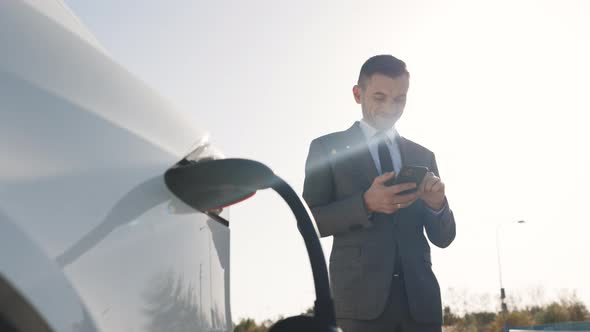 Caucasian Businessman Using Smartphone and Waiting Power Supply Connect to Electric Vehicles  alt