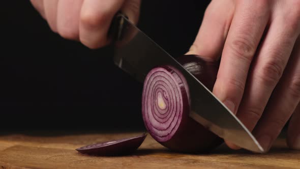 Hands cut red onions in kitchen on wooden board. Close up. 4k