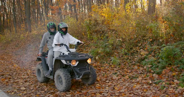 A Young Couple Rides an ATV Offroad in the Autumn Forest alt
