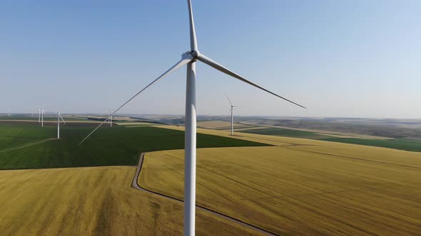 Aerial view raising up revealing static blades of a wind turbine in the middle of agricultural field alt
