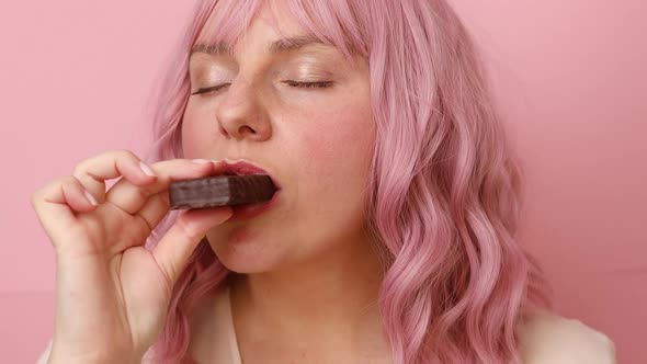 Young Woman Biting in a Pieace of Chocolate Waffle Candy Isolated Over Pink Background