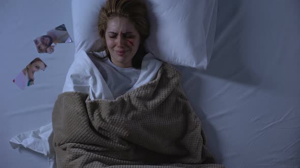 Crying Woman With Wound on Face Lying in Bed, Torn Photo Near Pillow, Breakup alt