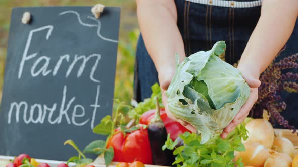 Farmer's Hands with a Head of Cabbage Over the Counter. Sale of Vegetables at the Farmers Market alt