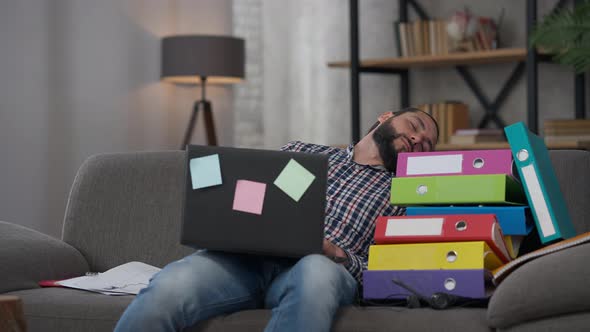 Handsome Tired Middle Eastern Man Napping in Home Office with Blurred Woman Passing at Background alt