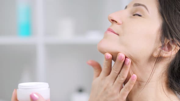 Closeup Relaxing Young Woman Enjoying Applying White Antiage Moisturizing Cream on Neck alt
