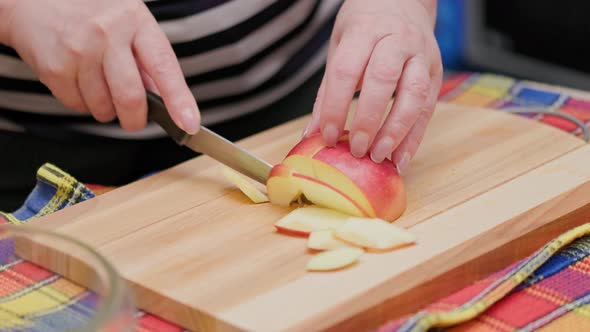Senior Woman Cut Red Apple with a Knife on Wooden Cutting Board on a Kitchen Table for Apple Pie alt