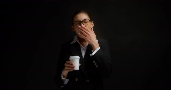 Woman in Office Clothes Yawns and Drinks Coffee From a White Paper Cup alt
