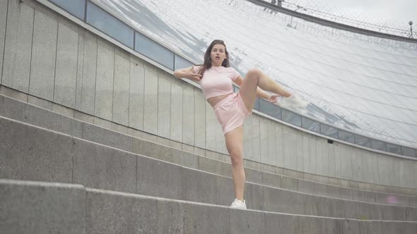 Wide Shot of Charming Brunette Caucasian Woman Stretching Leg Up Outdoors. Portrait of Confident alt