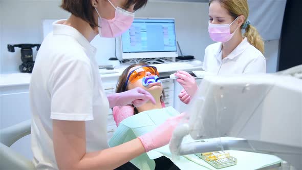 Woman Doctor Inserts A Dental Retractor Into Patient's Mouth Before Whitening Procedure.