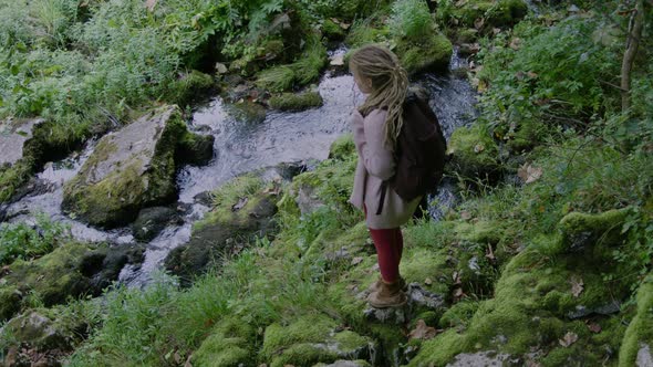 Travel woman with dreadlocks and backpack looks at the mountain alt