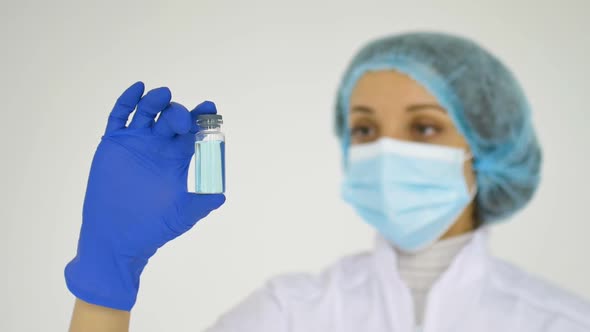 A Medical Worker Shows the Coronavirus Vaccine Wearing Blue Protective Gloves on White Background  alt