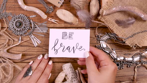 Hand with BE BRAVE card over a wooden table top view alt