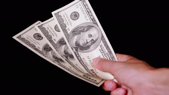 Hand Holding Three 100 Dollar Bills on Isolated Black Background alt