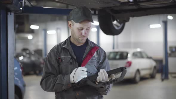 Portrait of Confident Serious Caucasian Man Looking at Car Bottom and Noting in Computer alt