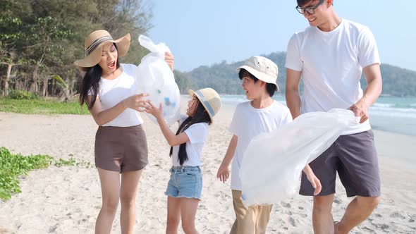 Asian Family volunteer picking up a plastic bottle on a beach with a sea to protect an environment