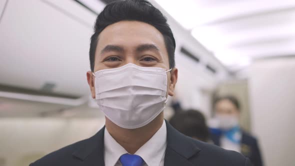 Asian male steward wearing medical face mask to prevent Coronavirus on airplane alt