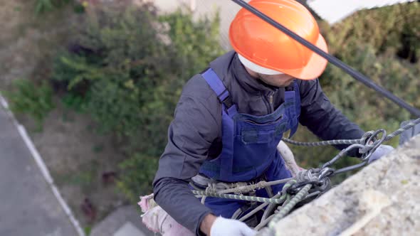 Highaltitude Work on Houses a Caucasian Male Worker Dressed in a Helmet Hangs on a Rope and Puts alt