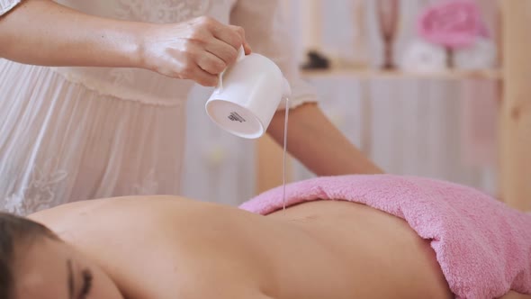 Caucasian Middleaged Female Pouring Massage Oil on Naked Woman Lying in Spa Salon in Slowmotion alt