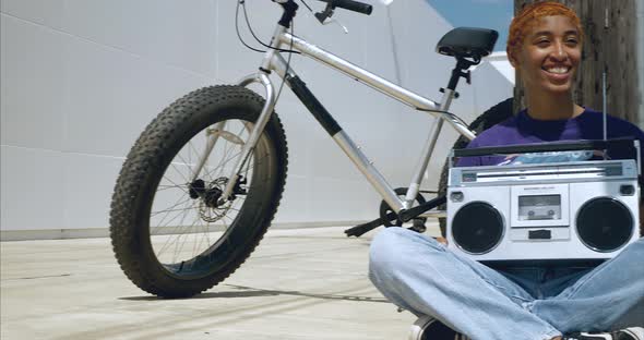 Panning shot of African American female holding boom box while sitting on ground alt